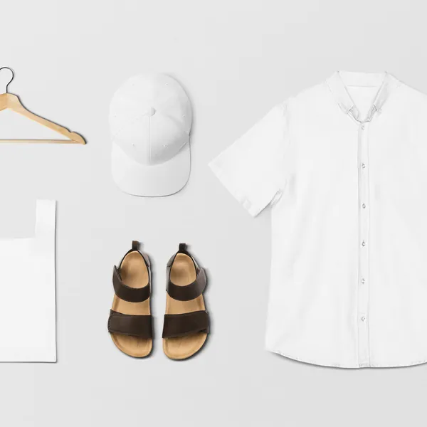 Flat lay of a white linen shirt with cap, sandals and tote